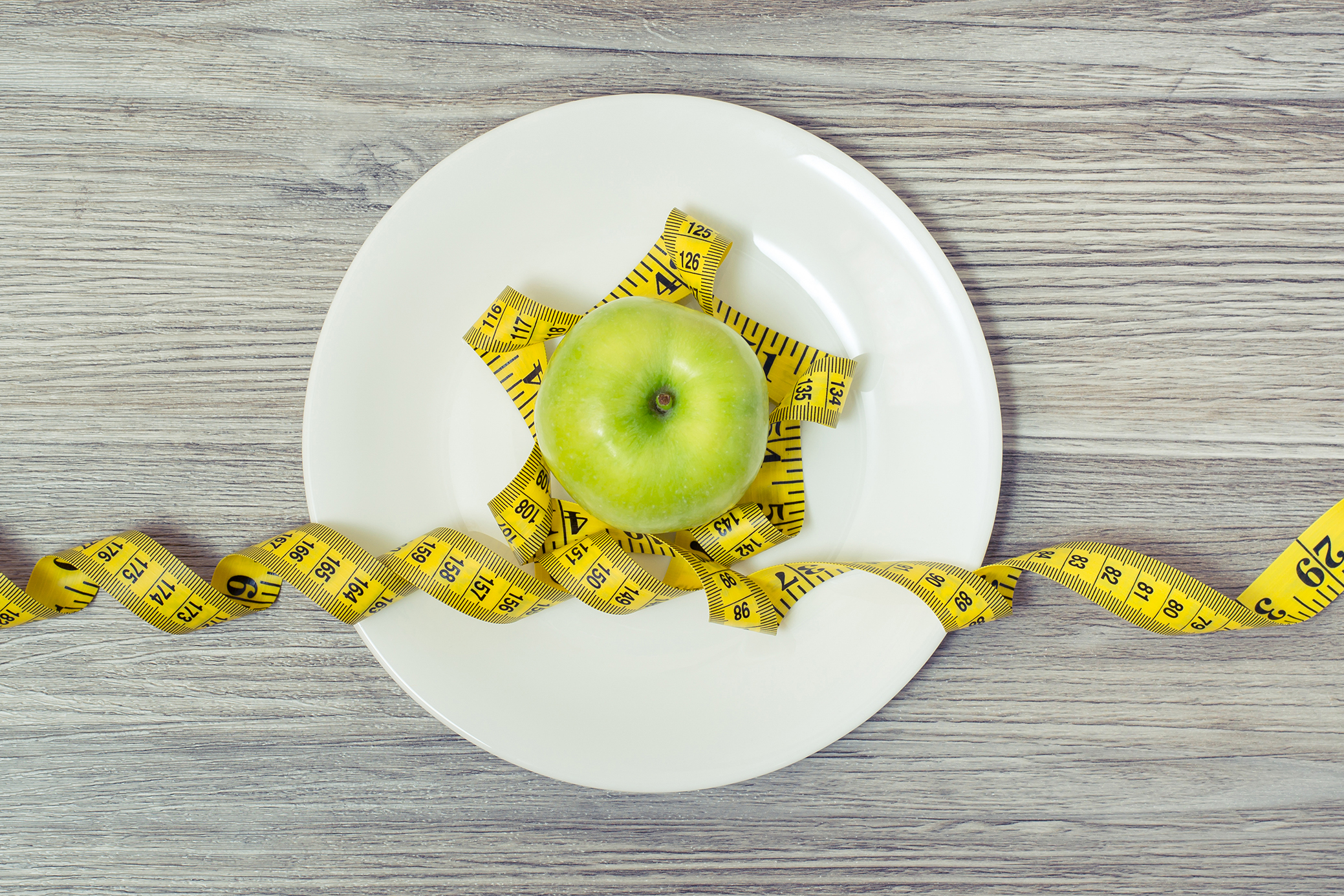 Top view on tape measure coiled around an apple on white plate